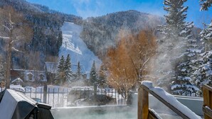 Area termale con una veranda in legno, vista su una montagna innevata e un edificio sullo sfondo.