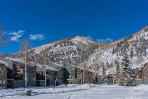 A row of cabins with a mountain backdrop, snow-covered ground, and clear blue sky.