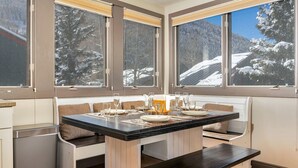 Zona pranzo con tavolo apparecchiato per quattro, ampie finestre con vista innevata e una zona con panche.