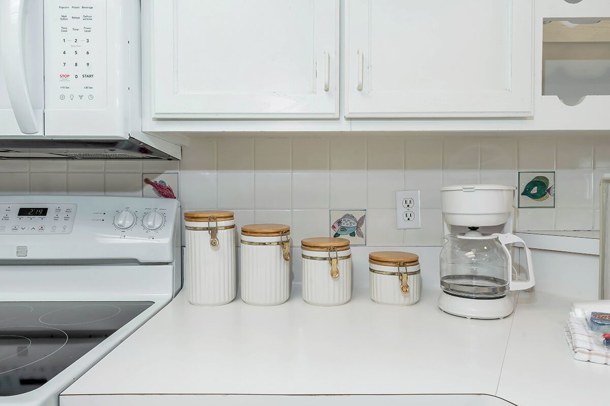 A kitchen with white cabinets, a white stove, and four jars with lids.