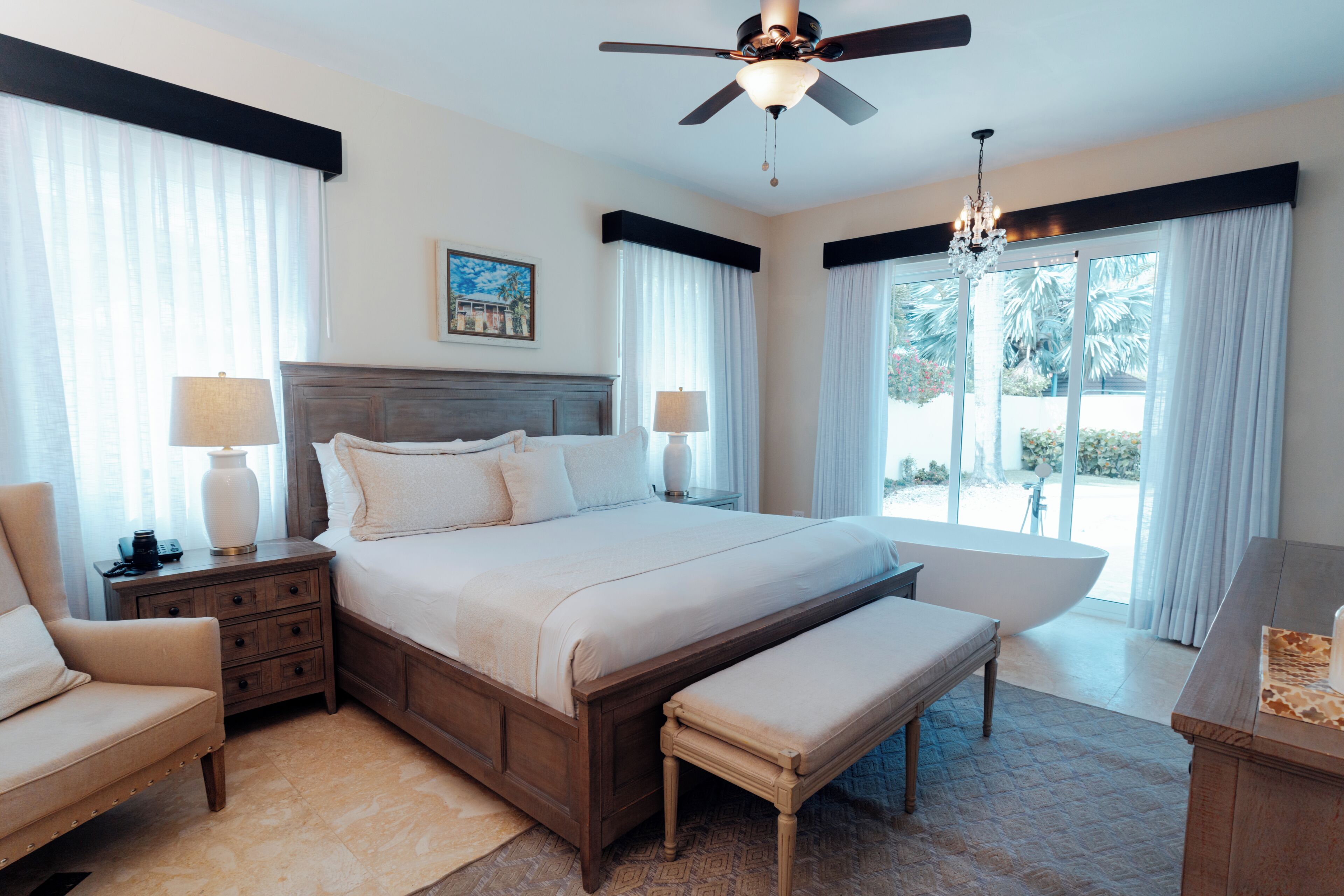 A spacious bedroom with a large bed, a bench, a chair, a nightstand, and a dresser.