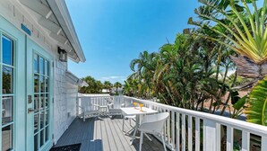 A wooden deck with a white railing, a table with two chairs, and a door with a window. - Crow's Nest Spinnakers Cottages: 250 Steps to Beach! Pool! (Holmes Beach)