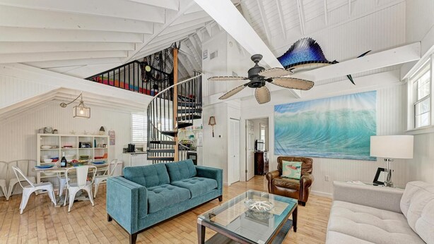 A spacious living room with a high ceiling, a staircase, and a large painting of a wave. - Crow's Nest Spinnakers Cottages: 250 Steps to Beach! Pool! (Holmes Beach)