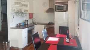 A compact kitchen with a microwave, stove, and refrigerator. There is a dining table with chairs and a small island with a sink and storage. - PINNACLE VALLEY Chalet 11 SHERPA'S REST (Merrijig)