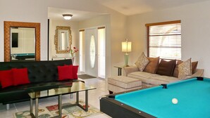 A living room with a pool table, a sofa, a glass coffee table, and a lamp. - Beautiful Water Views, 7-min Walk to Tigertail Beach entrance, 5 bikes, Hot Tub (Marco Island)