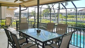 A glass-enclosed patio with a table and chairs, a ceiling fan, and a view of a pool and greenery. - Beautiful Water Views, 7-min Walk to Tigertail Beach entrance, 5 bikes, Hot Tub (Marco Island)