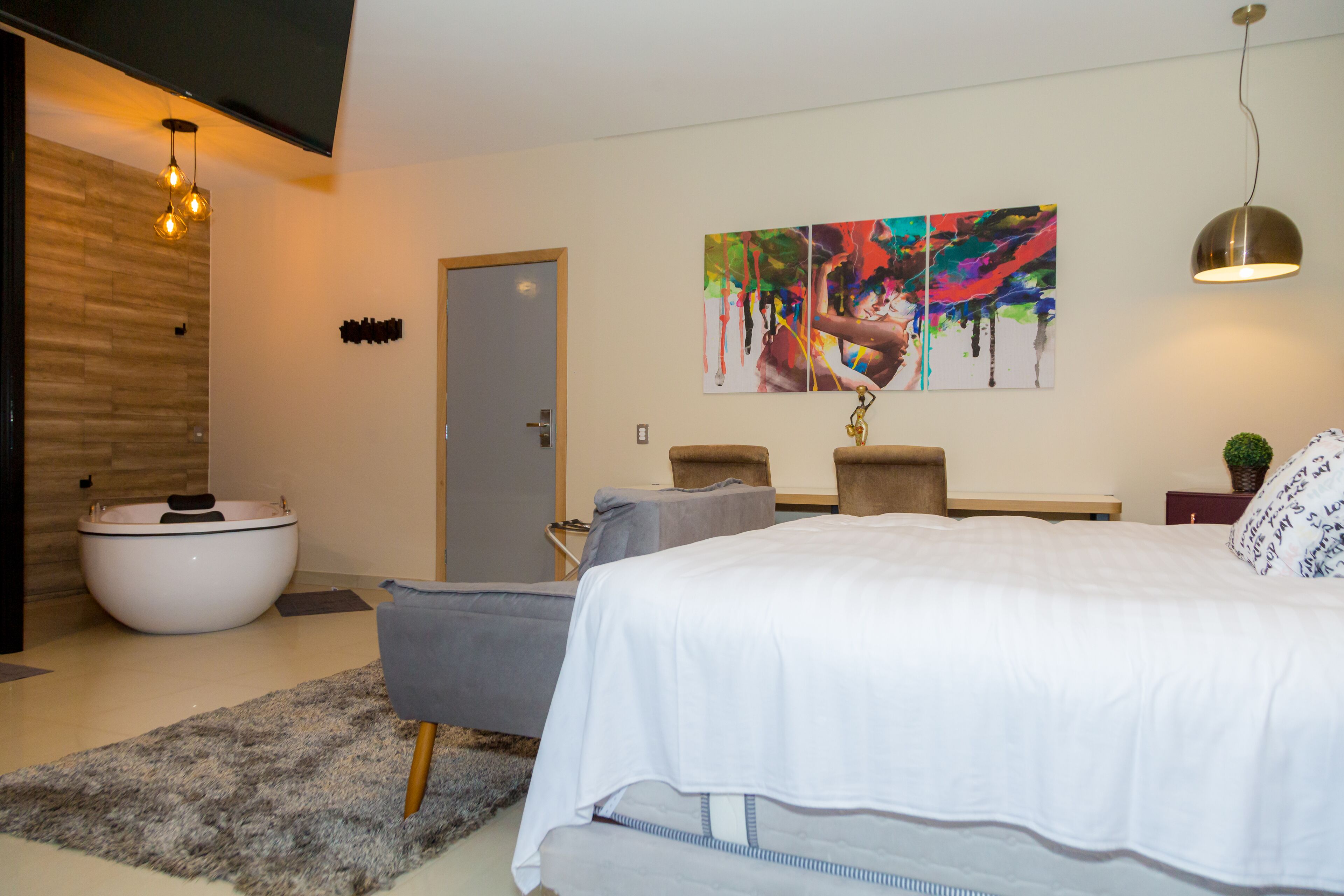 A modern bedroom with a large bed, a bathtub, and a gray sofa.