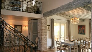 A spacious dining area with a high ceiling and exposed beams, a staircase with ornate metal railings, and a view of the outdoors through a glass door. - Mas in Eygalières with Heated Pool (Eygalières)