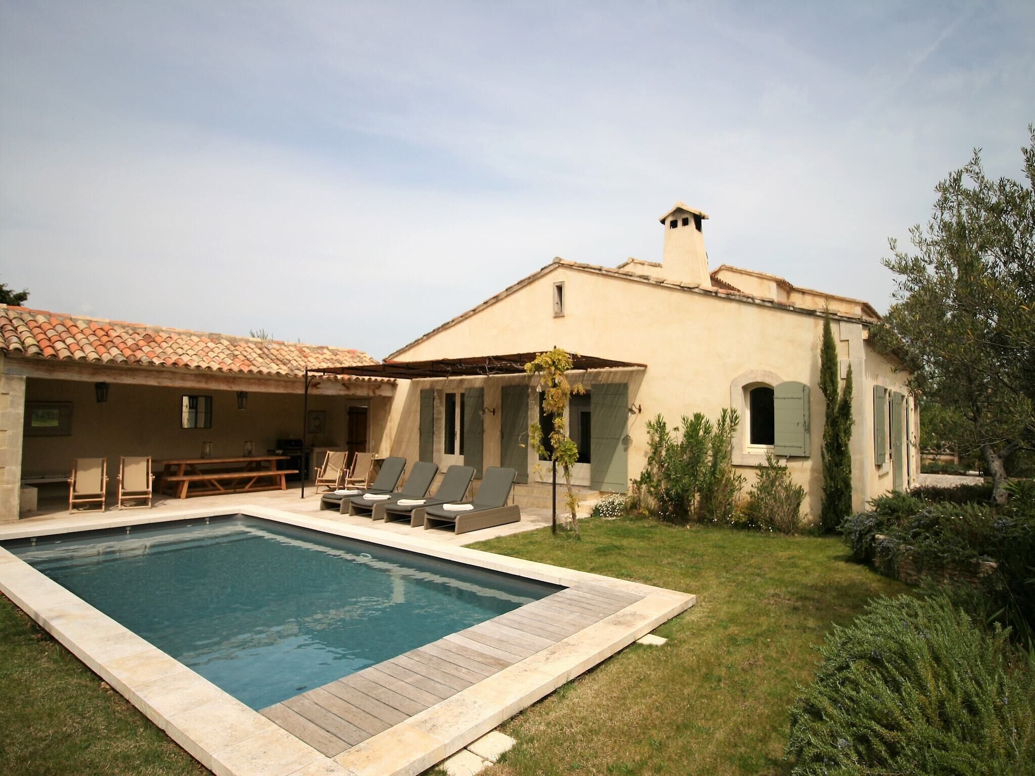 A poolside area with lounge chairs, a swimming pool, and a building with a tiled roof.
