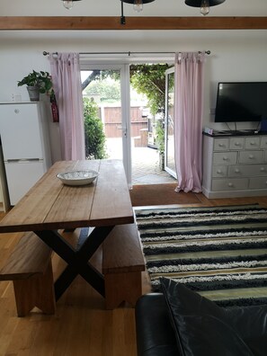 Een gezellige woonkamer met een houten tafel, een bank en een televisie. Er is een schuifpui die uitkomt op een tuin.