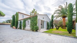 A modern house with a paved driveway, a well-maintained lawn, and a variety of trees including a tall palm. - Villa Saint-Tropez (Gassin)