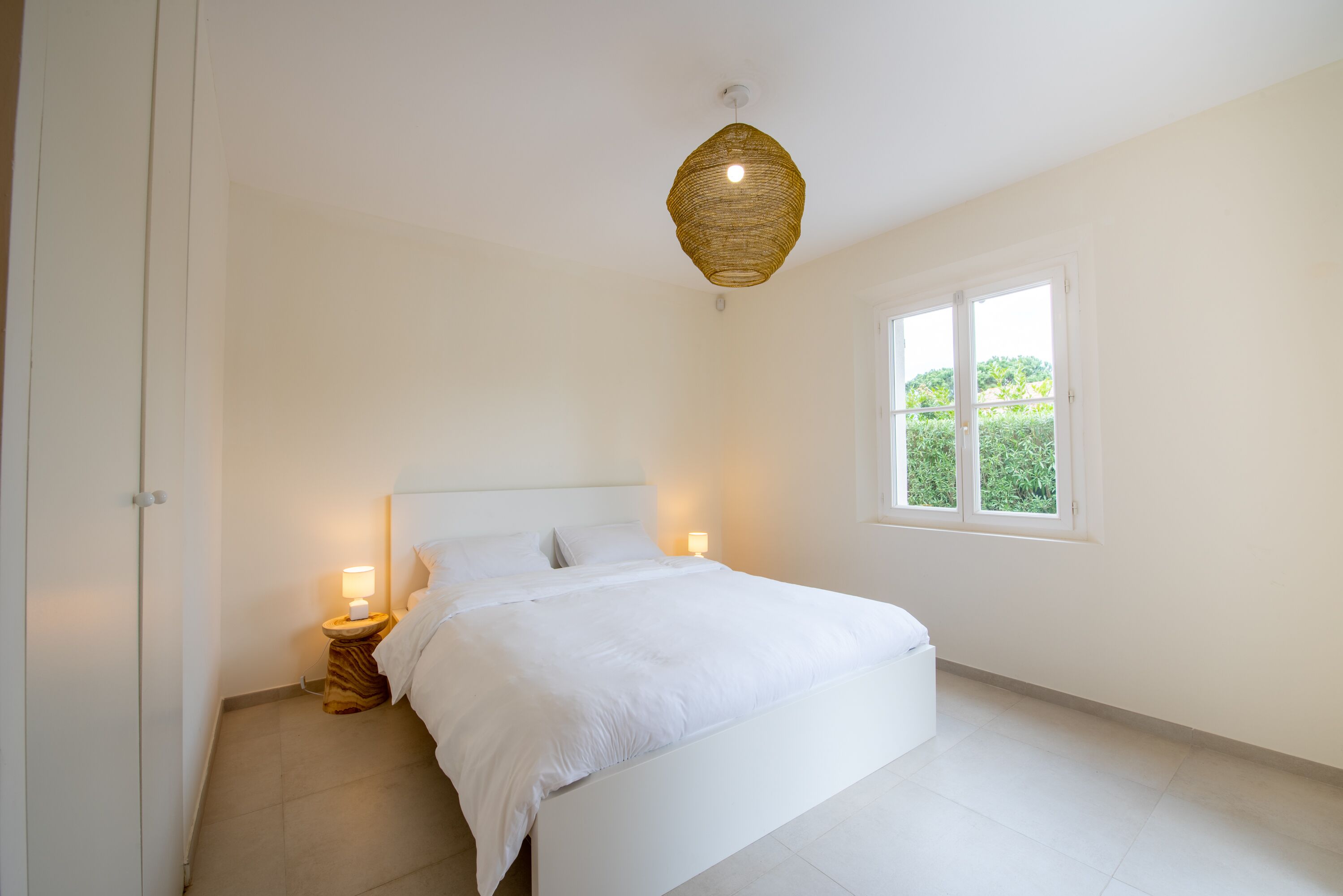 A bedroom with a large bed, bedside lamps, a window, and a ceiling light fixture.