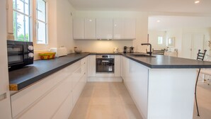 A modern kitchen with white cabinets, a black microwave, and a built-in oven. - Villa Saint-Tropez (Gassin)