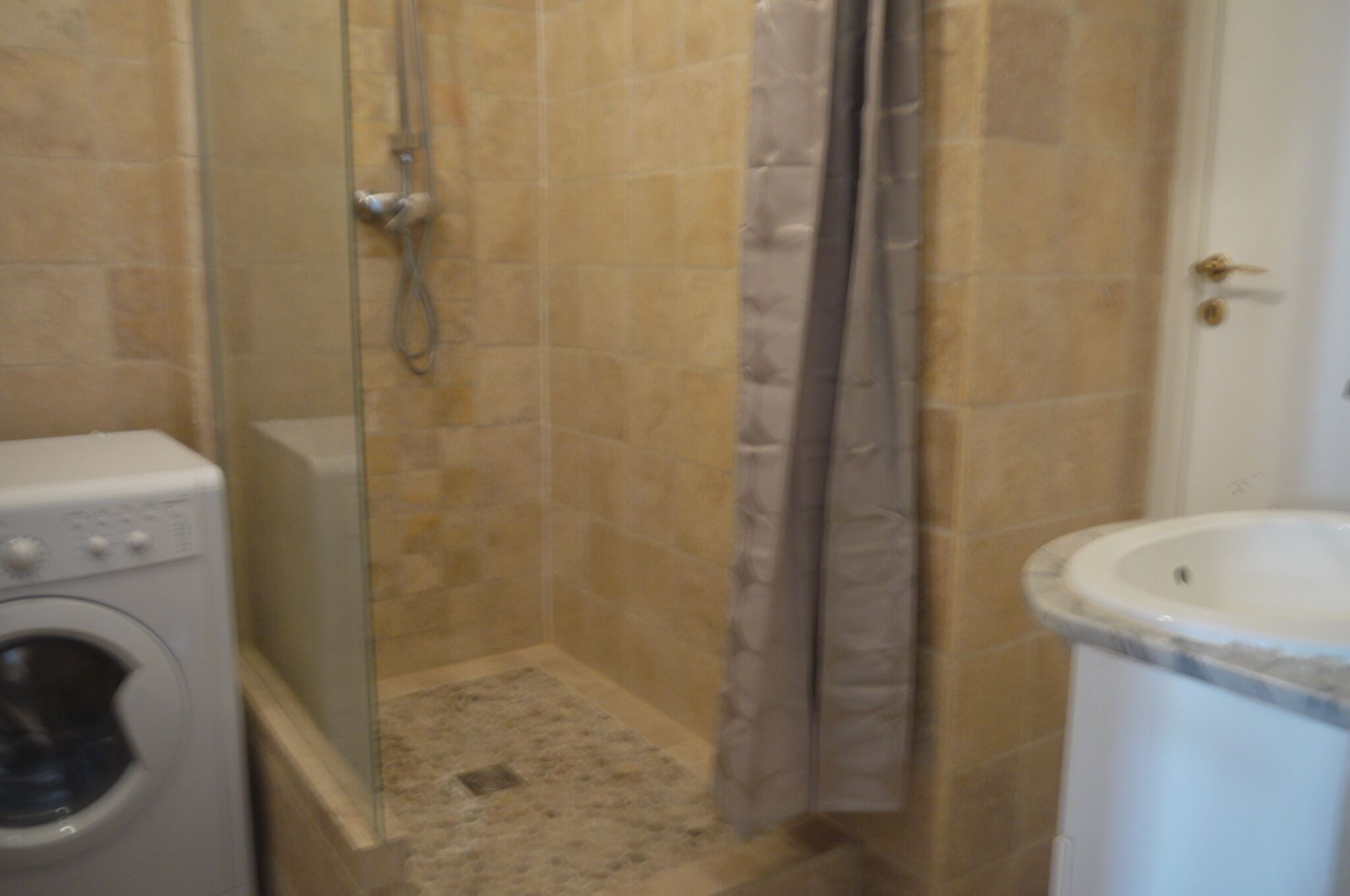A bathroom with a shower, a washing machine, and a sink.