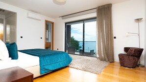 A modern bedroom with a large bed, a view of the sea, a balcony, and a chair. - Villa Vitória by LovelyStay (Funchal)
