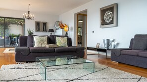 Una sala moderna con un sofá seccional, una mesa de centro de vidrio y una araña.