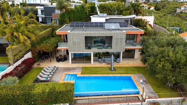 Una casa moderna de dos pisos con piscina, paneles solares y un jardín bien cuidado.