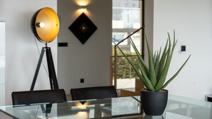 A modern interior with a glass table, black chairs, a potted aloe plant, a floor lamp, and a geometric wall decoration. - Villa Vitória by LovelyStay (Funchal)