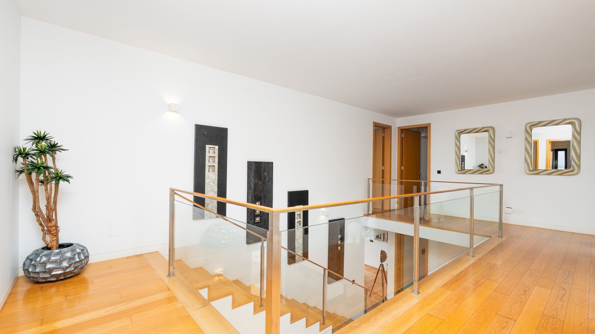 Un intérieur moderne avec un escalier, une balustrade en verre, un plancher en bois et un décor minimaliste.