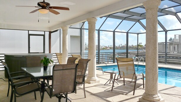 Área de piscina no terraço, com mesa, cadeiras, ventilador de teto e vista para a água.