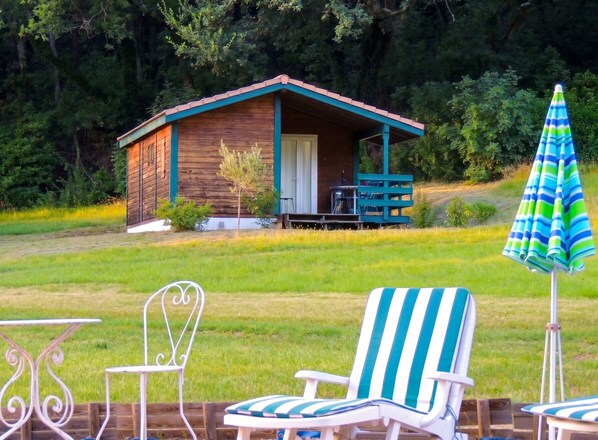 A wooden cabin with a porch, surrounded by a grassy area and trees. - Homerez - Chalet in Les Tourettes (Les Tourettes)