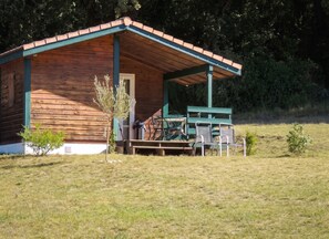 A wooden cabin with a covered porch, a small table, and chairs. - Homerez - Chalet in Les Tourettes (Les Tourettes)