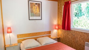 Un dormitorio con cabecera de madera, una cama con almohadas blancas, una colcha roja, una obra de arte enmarcada en la pared y una ventana con cortina roja.