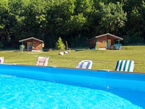 A swimming pool with lounge chairs, two wooden cabins, and a grassy area with trees in the background. - Homerez - Chalet in Les Tourettes (Les Tourettes)