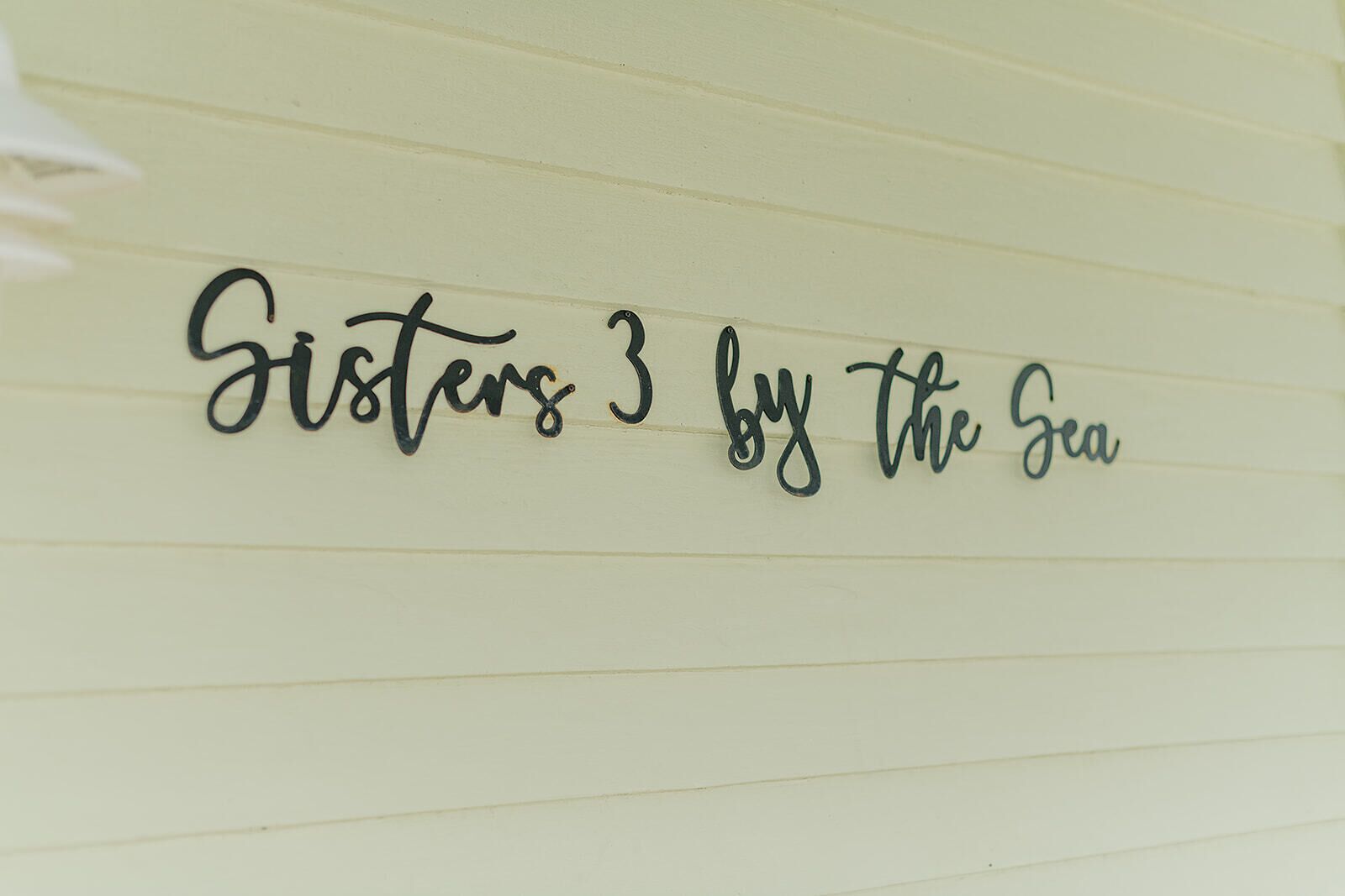A wall with the text 'Sisters 3 by the Sea' in a cursive font.