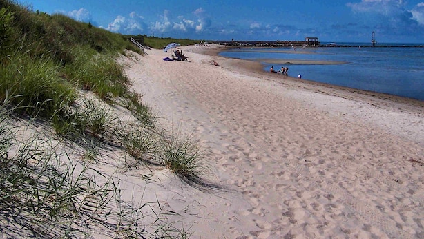 A sandy beach with dunes, a pier, and a lighthouse in the distance. - Sisters 3 by the Sea, 400 Feet To The Beach (Cape Charles)