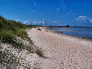 A sandy beach with dunes, a pier, and a lighthouse in the distance.