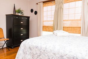 A bedroom with a bed, a dresser, a chair, and a window with curtains.