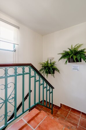 A staircase with a green metal railing, a white wall, and a tiled floor.