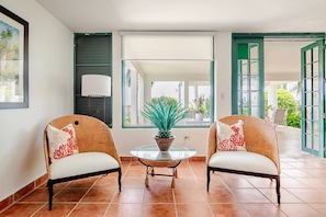 A room with two wicker chairs, a glass table with a potted plant, and a view through a window.