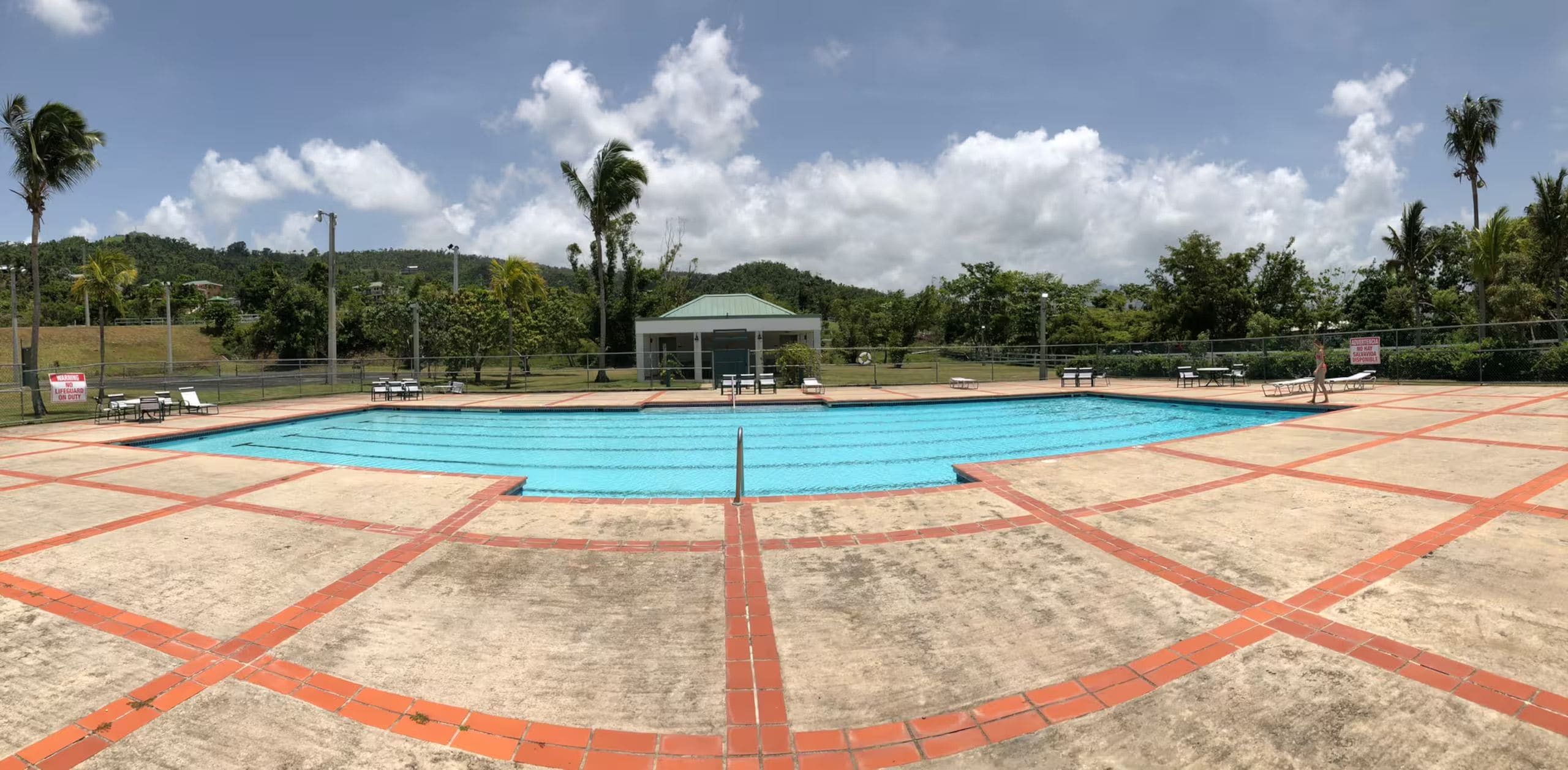 A swimming pool with a lifeguard station, surrounded by a fenced area with lounge chairs and a pavilion.