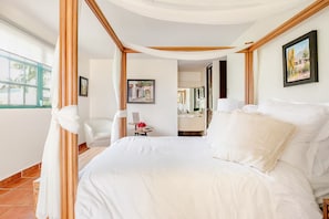 A hotel room with a large bed, a sitting area with a chair, a small table with a vase, and a view of the outside.