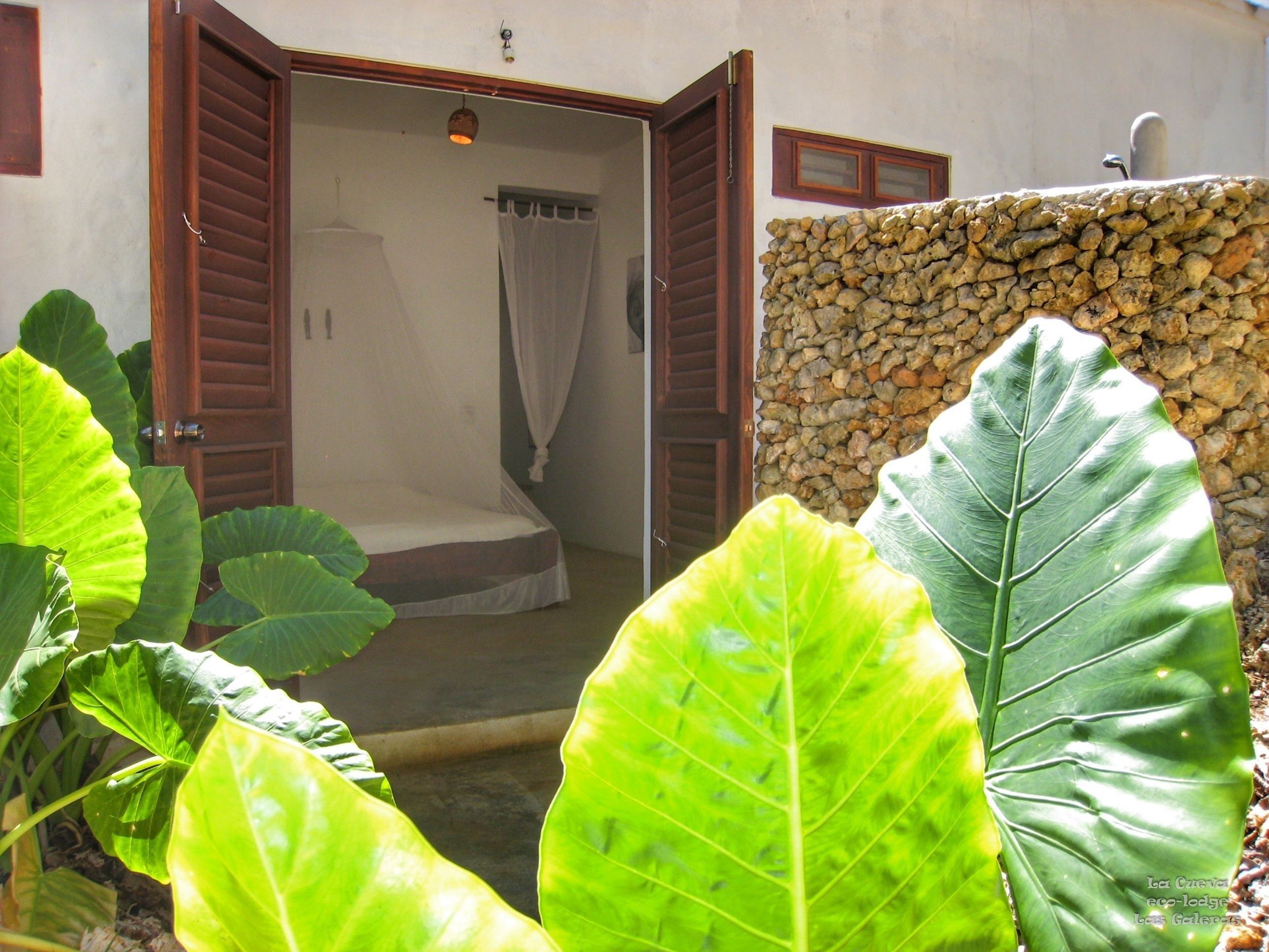 A room with a bed, a wooden door, and a stone wall.