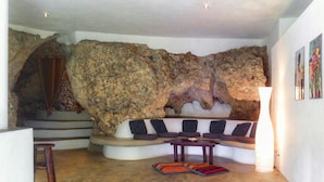 A living room with a stone wall, a curved sofa, a small table, and a stool. - La Cueva Eco-Lodge (Las Galeras)