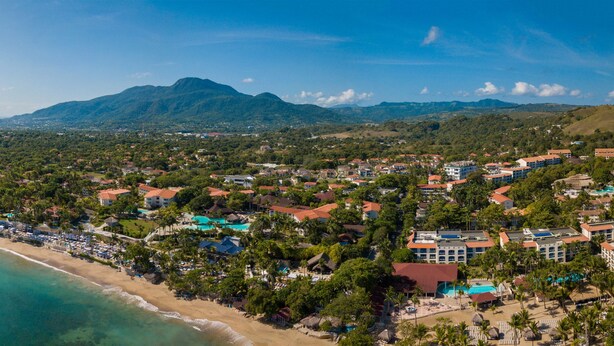 Ein Luftbild eines Küstenresorts mit Strandhäusern, einem Berg im Hintergrund und blauem Himmel.