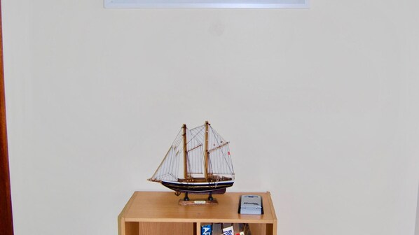 Un modèle de bateau, posé sur une étagère en bois, devant un mur uni.