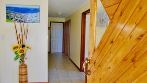 Ein Flur mit einer Holztür, einem Fliesenboden und einem an der Wand hängenden Bild eines Küstenortes.