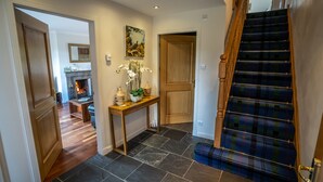 Un escalier recouvert d’une moquette à carreaux, une porte en bois et une console sur laquelle est posé un vase de fleurs.