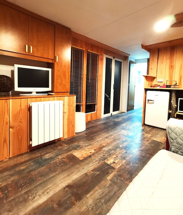A compact kitchen with wooden cabinets, a built-in TV, a refrigerator, and a radiator.