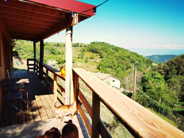A wooden deck with a view of a green landscape, a table, and a chair.