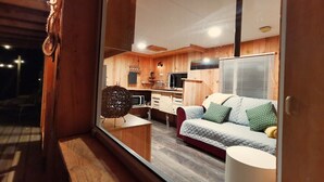 A cozy interior with a wooden floor, a sofa with cushions, a small table, and a kitchen area with cabinets and a microwave.