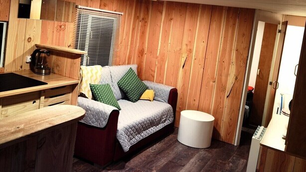 A compact room with a kitchenette, a sofa with patterned cushions, and a small round table.