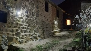 A stone building with a dirt path leading to a lit entrance.