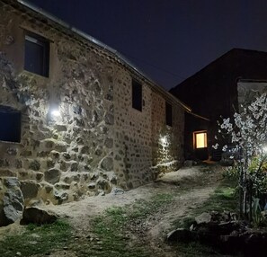 A stone building with a dirt path leading to a lit entrance.