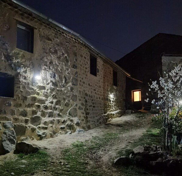 A stone building with a dirt path leading to a lit entrance.