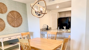 A dining area with a wooden table and chairs, a chandelier, and a kitchen in the background. - Beachfront 1BR/2BA Villa, Pet Friendly, Stunning Views, Amenity Access included (Seabrook Island)